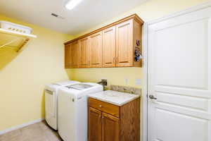 Laundry area featuring washing machine and clothes dryer, cabinet space, and light tile patterned floors