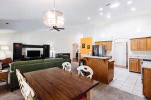 Dining area featuring arched walkways, a ceiling fan, light tile patterned floors, light colored carpet, and high vaulted ceiling