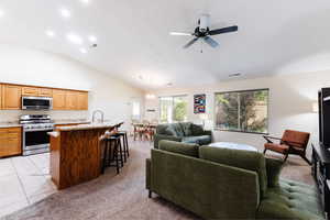 Living room with light carpet, vaulted ceiling, light tile patterned floors, and a ceiling fan