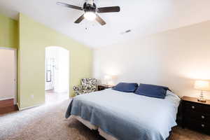 Bedroom with arched walkways, carpet flooring, lofted ceiling, connected bathroom, and a ceiling fan