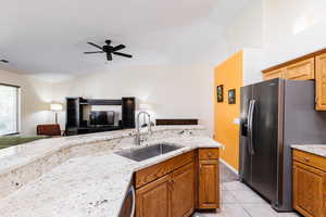 Kitchen featuring stainless steel refrigerator with ice dispenser, brown cabinetry, light stone countertops, light tile patterned flooring, and open floor plan