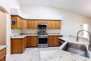Kitchen featuring light stone counters, brown cabinets, appliances with stainless steel finishes, light tile patterned flooring, and lofted ceiling