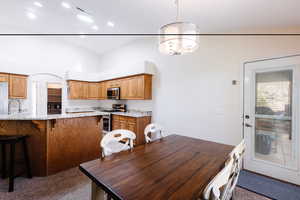 Kitchen with dark carpet, a kitchen breakfast bar, vaulted ceiling, light stone countertops, and appliances with stainless steel finishes