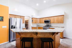Kitchen featuring stainless steel appliances, a breakfast bar area, a kitchen island with sink, light stone countertops, and high vaulted ceiling