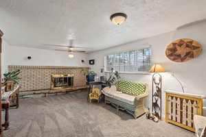Living room featuring carpet flooring, a textured ceiling, a brick fireplace, and a ceiling fan