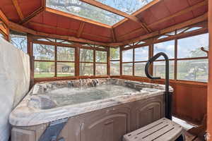 Sunroom with a jacuzzi, a skylight, plenty of natural light, lofted ceiling, and wooden walls