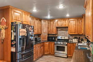 Kitchen featuring stainless steel appliances, dark stone countertops, brown cabinetry, backsplash, and light wood-type flooring