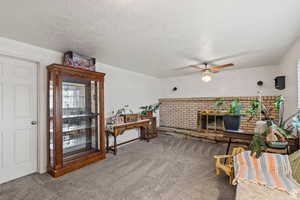 Sitting room featuring carpet flooring, a fireplace, a ceiling fan, and a textured ceiling