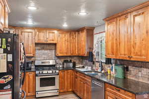 Kitchen with appliances with stainless steel finishes, backsplash, dark stone counters, a textured ceiling, and brown cabinetry