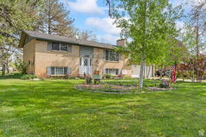 View of front of home with a front yard, a chimney, and brick siding