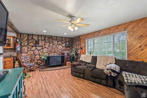 Living area with a wood stove, a textured ceiling, wood finished floors, wooden walls, and ceiling fan