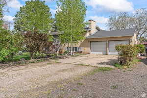 View of front of property featuring concrete driveway, a garage, brick siding, a chimney, and roof with shingles