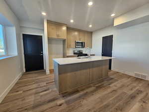 Kitchen featuring recessed lighting, a kitchen island with sink, appliances with stainless steel finishes, light wood-style flooring, and light brown cabinetry