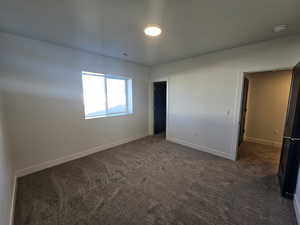Unfurnished bedroom featuring dark colored carpet and baseboards