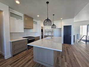 Kitchen with white cabinetry, gas stove, an island with sink, dark wood finished floors, and recessed lighting