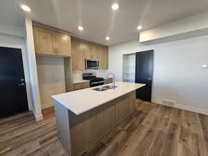 Kitchen featuring recessed lighting, appliances with stainless steel finishes, a center island with sink, dark wood-style flooring, and light stone counters
