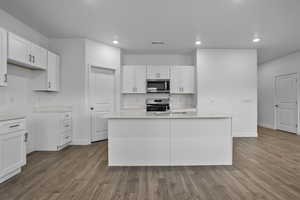 Kitchen with white cabinetry, light wood-style floors, an island with sink, appliances with stainless steel finishes, and recessed lighting