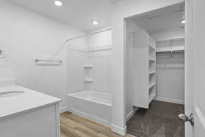 Full bathroom with vanity, a walk in closet, washtub / shower combination, light wood-type flooring, and recessed lighting