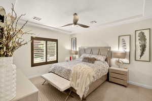 Carpeted bedroom featuring ceiling fan and a tray ceiling