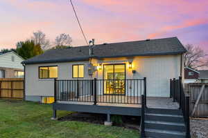 Back of house at dusk with brick siding, a wooden deck, and a shingled roof