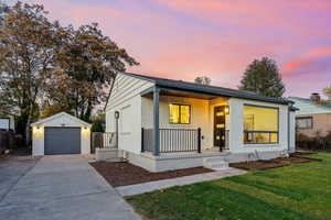 View of front of property with a porch, an outdoor structure, a lawn, driveway, and brick siding