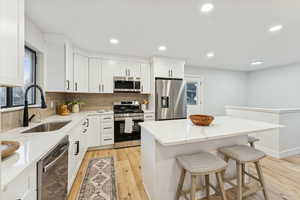 Kitchen featuring decorative backsplash, a breakfast bar, stainless steel appliances, light wood-style floors, and light stone countertops