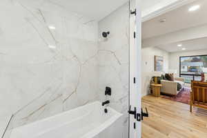 Ensuite bathroom with a combined bath / shower with marble appearance, light wood finished floors, and recessed lighting