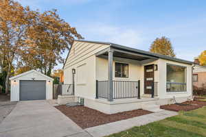 View of front of property featuring an outbuilding, driveway, brick siding, covered porch, and a detached garage