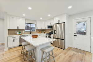 Kitchen featuring appliances with stainless steel finishes, tasteful backsplash, a kitchen breakfast bar, white cabinets, and light wood finished floors