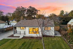 Back of property at dusk featuring roof with shingles, a yard, brick siding, and a patio