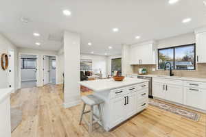 Kitchen featuring tasteful backsplash, white cabinetry, a kitchen bar, light wood-style floors, and recessed lighting