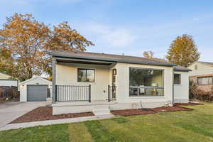 View of front of property with brick siding, a front yard, concrete driveway, an outdoor structure, and roof with shingles