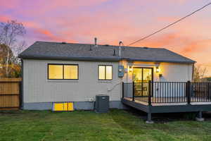 Back of house at dusk featuring brick siding, a deck, and a shingled roof