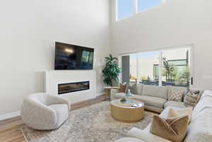 Living area featuring wood finished floors, a glass covered fireplace, and a high ceiling
