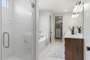 Bathroom featuring a walk in closet, a soaking tub, vanity, light marble finish flooring, and a marble finish shower