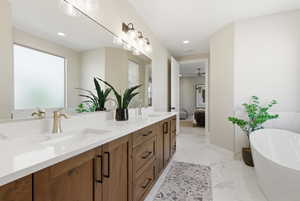 Full bathroom featuring light marble finish flooring, a freestanding bath, double vanity, ensuite bathroom, and ceiling fan