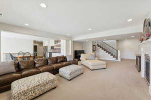 Living area with a glass covered fireplace, recessed lighting, light carpet, and stairs