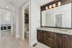 Full bathroom featuring double vanity, a stall shower, washing machine and dryer, recessed lighting, and light wood-style flooring