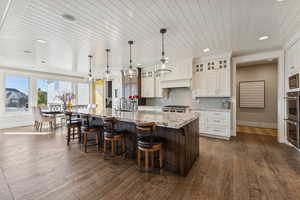 Kitchen featuring a large island with sink, backsplash, a kitchen breakfast bar, light stone countertops, and wooden ceiling