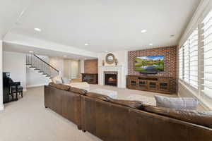 Living room featuring light colored carpet, a warm lit fireplace, recessed lighting, brick wall, and stairway