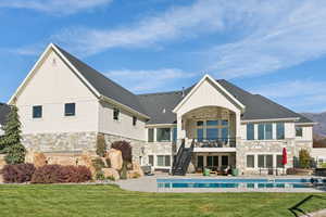 Rear view of house featuring stone siding, stairs, a lawn, a balcony, and a patio area