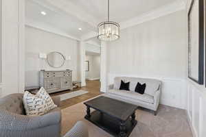 Living room featuring a chandelier, beam ceiling, a decorative wall, crown molding, and wainscoting
