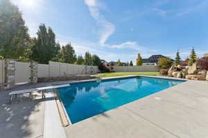 View of pool with a diving board, a patio area, and a fenced backyard