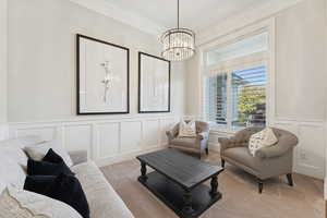 Living area with a decorative wall, crown molding, wainscoting, carpet floors, and a chandelier