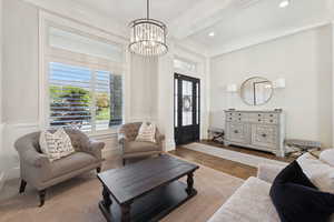 Living room with beam ceiling, a chandelier, crown molding, and wood finished floors