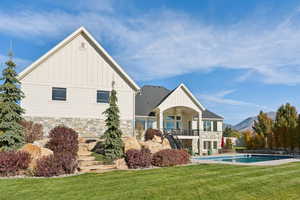 Rear view of property featuring stone siding, board and batten siding, a yard, an outdoor pool, and a mountain view