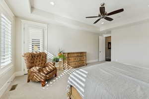 Carpeted bedroom with a raised ceiling, recessed lighting, and ceiling fan