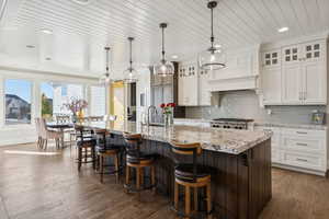 Kitchen featuring decorative backsplash, a breakfast bar, glass insert cabinets, dark brown cabinets, and light stone counters