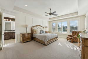 Bedroom with a tray ceiling, light colored carpet, ceiling fan, connected bathroom, and recessed lighting
