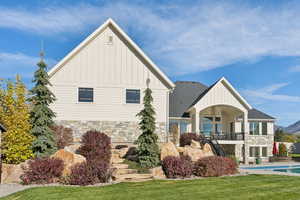 Back of property featuring stone siding, board and batten siding, stairway, a patio area, and an outdoor pool